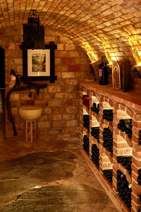 Stimmungsvolles Ambiente im Weinkeller mit Tonnengewölbe und gemauerten Weinfächern und Felsplatte als Fußboden